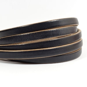 May include: Black leather cord with a tan edge. The cord is rolled up and shows the edge of the leather.