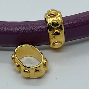 May include: Two gold-toned metal bead charms with a circular design. The charms have a smooth, shiny finish and are decorated with raised dots.