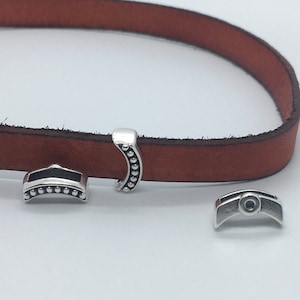 May include: Three silver metal clasps for leather straps. The clasps are in the shape of a half-circle and have a beaded edge. One clasp has a small circle in the centre.