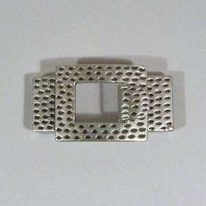 May include: Silver-toned metal buckle with a textured, geometric design. The buckle has a square shape with a smaller square opening in the center.