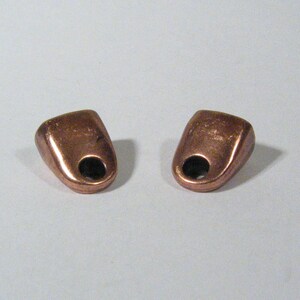 May include: Two small copper-colored metal toggles with a hole in the center of each. The toggles are slightly rounded on the top and bottom.