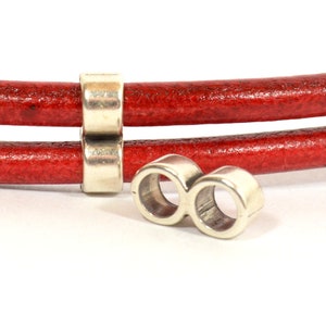May include: Silver metal bead with two holes for leather cord. The bead is designed to be used as a spacer or connector for leather bracelets or necklaces.