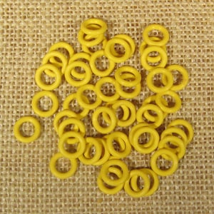 May include: A scattering of small, yellow, ring-shaped objects on a textured, tan surface. The rings are uniform in size and shape, and appear to be made of a solid material. The image is well-lit, showing the details of the rings.