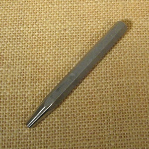 May include: A silver metal punch tool with a pointed tip and a hexagonal shaft.