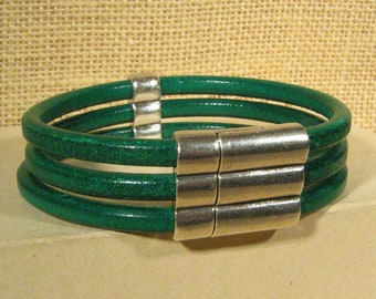 May include: A green leather bracelet with a silver magnetic clasp. The bracelet is made of four strands of leather.