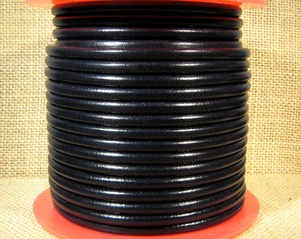 May include: A black leather cord wound on a spool with a red plastic base. The cord is tightly packed, forming a cylindrical shape. The background is a neutral tan fabric.