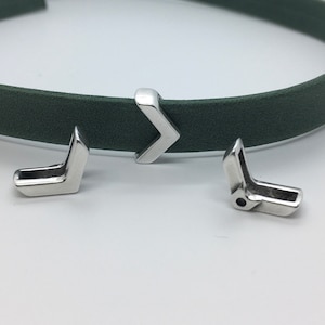 May include: Three silver metal arrow-shaped clasps for a leather strap. The clasps are in different positions, one is on a green leather strap.