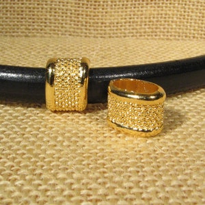 May include: Two gold-toned metal beads with a textured surface. The beads are designed to be used as a spacer on a leather cord or bracelet.