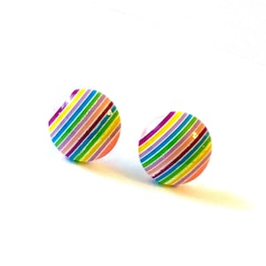 May include: Two round stud earrings with a colorful striped pattern. The earrings feature a vibrant array of colors, including pink, yellow, blue, and purple, arranged in diagonal stripes. The earrings are set against a white background.