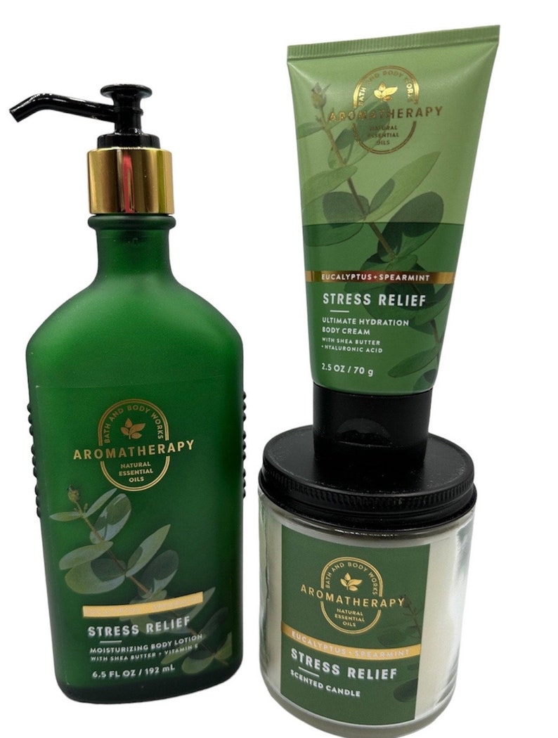 May include: A set of three bath and body products in a green and white color scheme. The products are a body lotion, a body cream, and a scented candle. All three products feature the text "Stress Relief" and "Eucalyptus Spearmint" and are labeled "Bath and Body Works Aromatherapy".