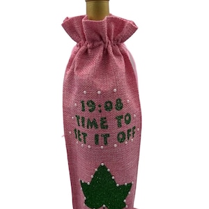 May include: Pink burlap wine bottle bag with green glitter ivy leaf and the text "19:08 Time to Set It Off" in white.
