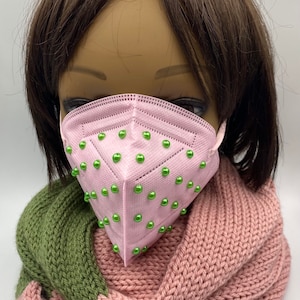 May include: Pink face mask with green beads. The mask has a diamond shape and is made of a soft, breathable material.