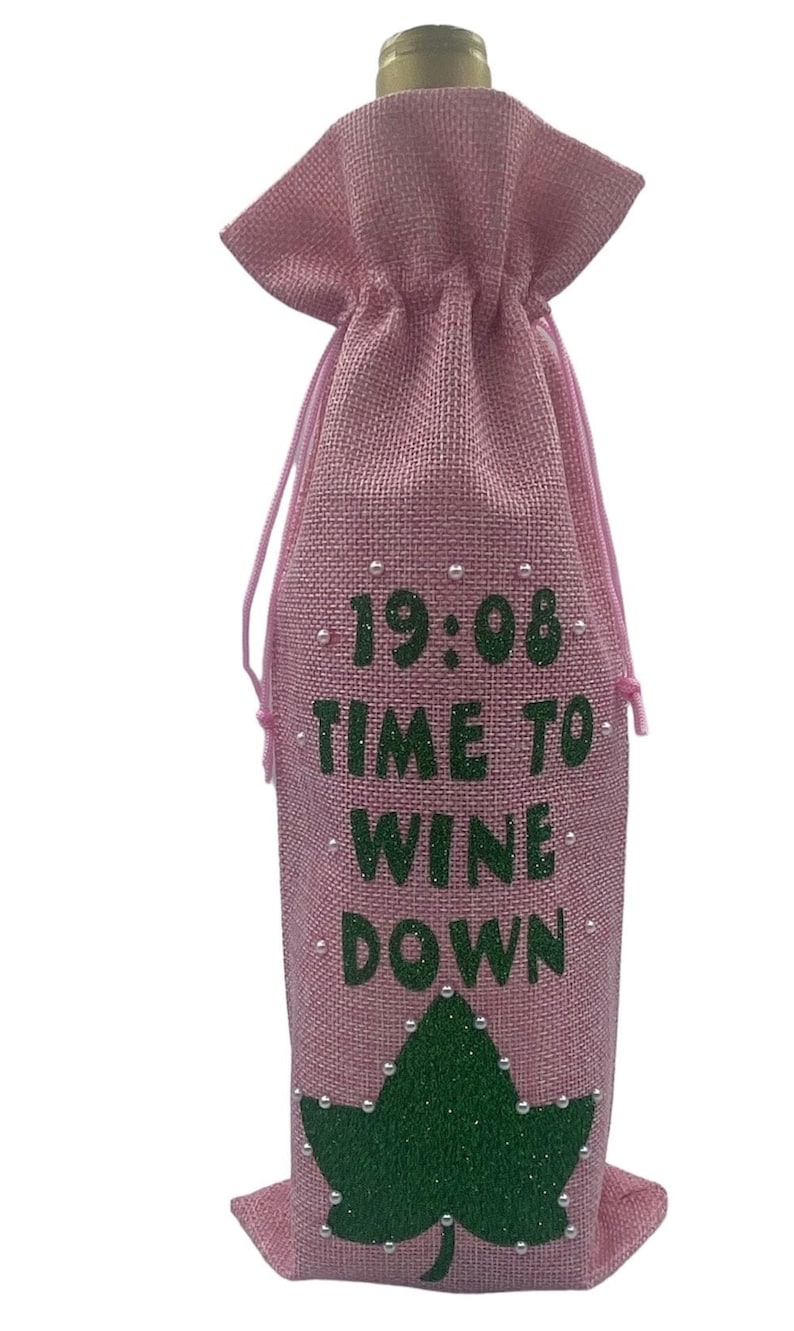 May include: Pink burlap wine bottle bag with green glitter text that reads "19:08 Time to Wine Down" and a green glitter leaf with white pearl accents.
