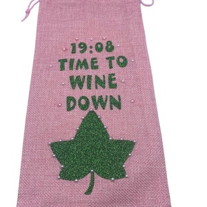 May include: Pink burlap wine bag with a green glitter leaf and white beads. The bag has the text "19:08 TIME TO WINE DOWN" printed on it.