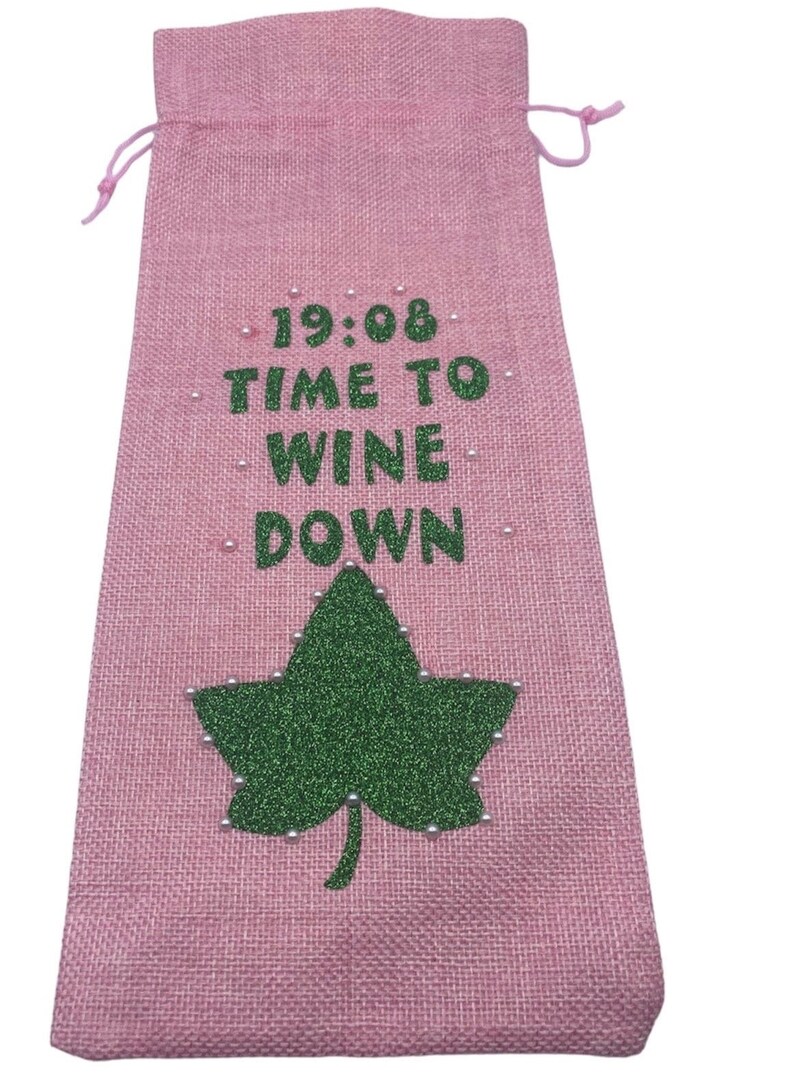 May include: Pink burlap wine bag with a green glitter leaf and white beads. The bag has the text "19:08 TIME TO WINE DOWN" printed on it.