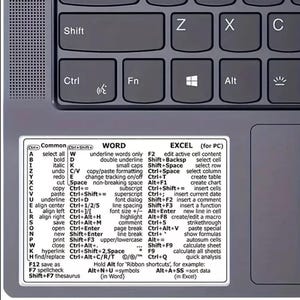 May include: A laptop keyboard with a sticker detailing Word and Excel keyboard shortcuts. The sticker is white with black text. The keyboard is grey.