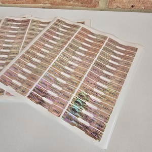 Può includere: Fogli di adesivi ologrammati con garanzia annullata se rimossi. Ogni adesivo ha un numero di serie univoco e il testo "WARRANTY VOID IF REMOVED". Gli adesivi sono rettangolari con angoli arrotondati.