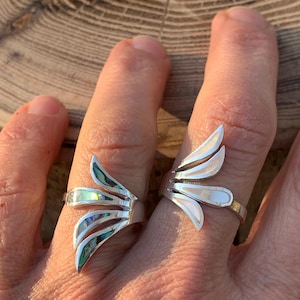 Peut inclure: Deux bagues en argent avec un design en éventail composé de trois segments distincts. La bague de gauche présente des incrustations de nacre d'ormeau irisée, tandis que celle de droite comporte des incrustations de nacre blanche lisse.