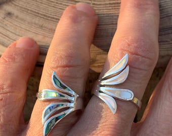 May include: Two silver rings featuring a fan-like design with three distinct segments. The ring on the left contains iridescent abalone shell inlays, while the ring on the right features smooth, white mother-of-pearl inlays set into the metal.