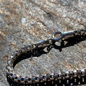 May include: A silver chain necklace with a box chain design and a lobster clasp closure.