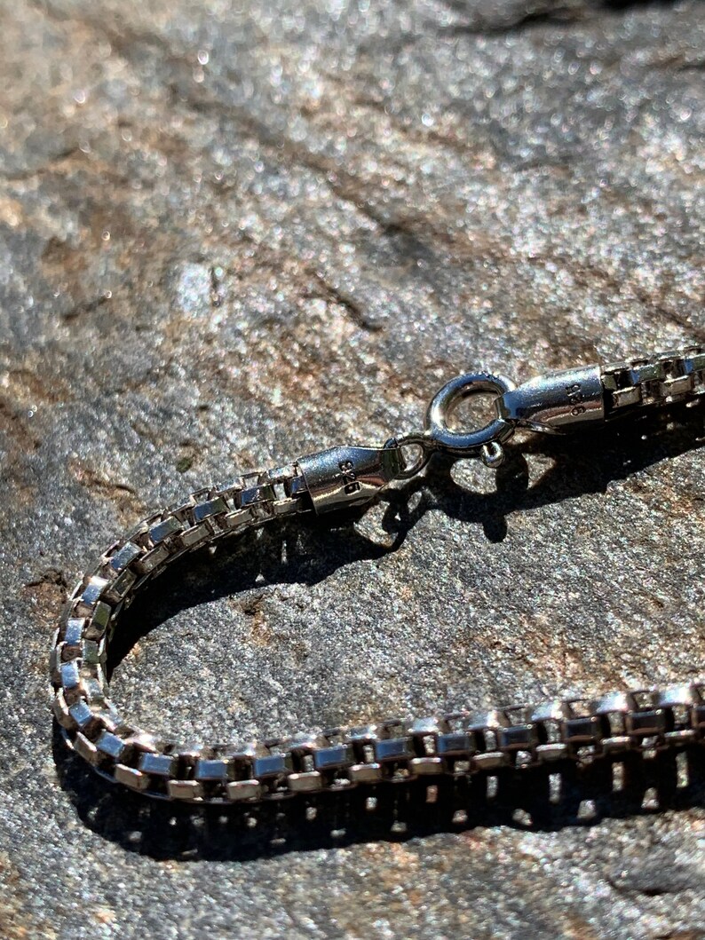 May include: A silver chain necklace with a box chain design and a lobster clasp closure.