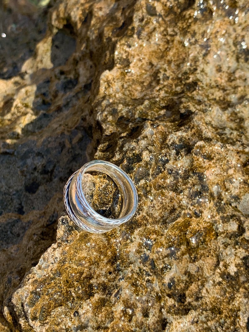 May include: Two silver rings stacked on top of each other on a brown, textured rock.