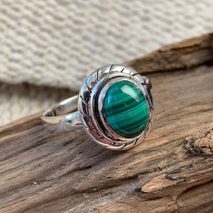 Op de afbeelding: Een zilveren ring met een groene malachiet steen gezet in een decoratieve bezel. De ring heeft een gedraaide band.