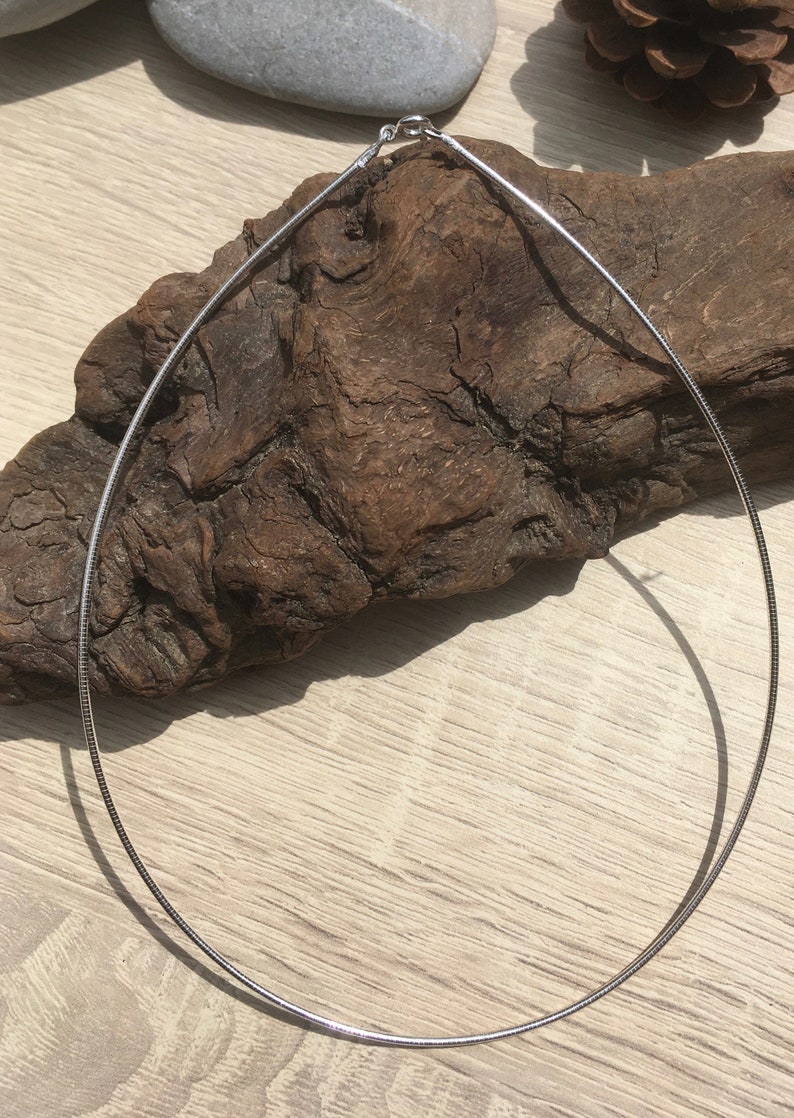 Op de afbeelding: Een zilveren slangenkettingketting op een houten oppervlak.
