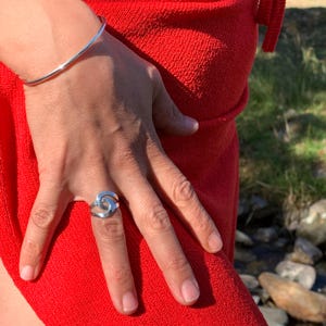 Può includere: Un anello d'argento con un design a spirale e un braccialetto d'argento abbinato. I gioielli sono esposti su uno sfondo rosso vibrante, creando un contrasto sorprendente. L'anello è il punto focale, mostrando i suoi dettagli intricati.