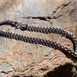 May include: A silver chain necklace with a box clasp. The chain is made of small, square links.