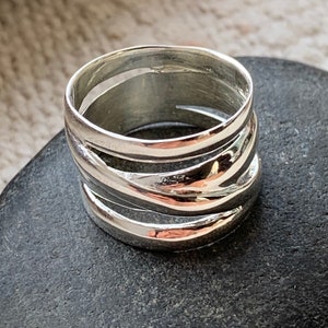 Pu&ograve; includere: Un anello d'argento con una fascia larga che presenta pi&ugrave; linee ondulate sovrapposte.