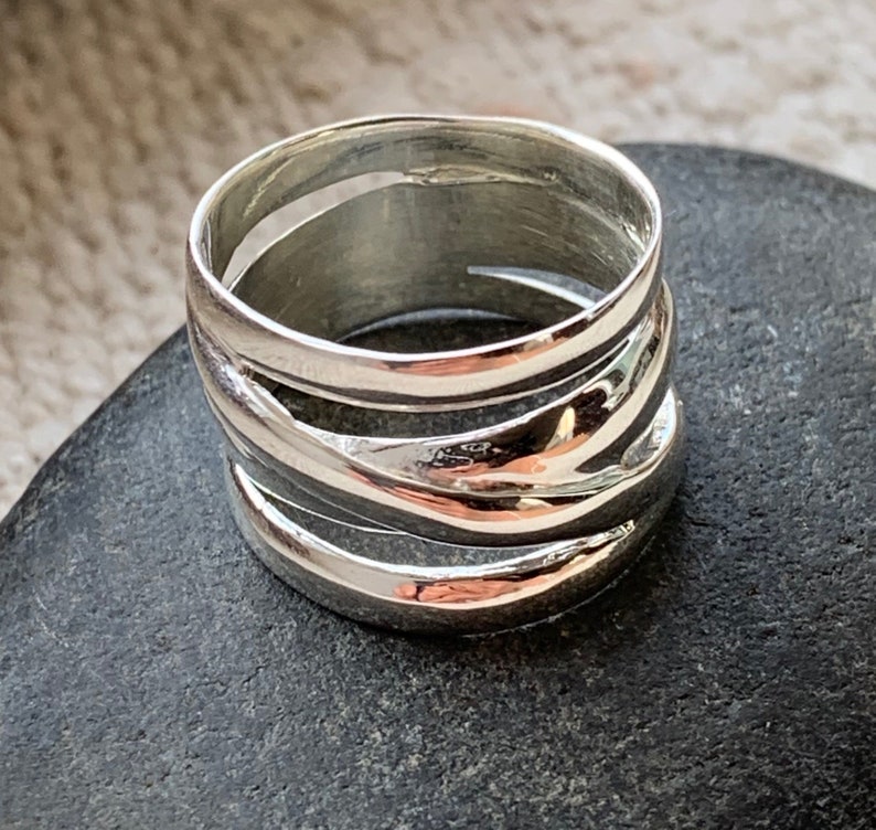 Pu&ograve; includere: Un anello d'argento con una fascia larga che presenta pi&ugrave; linee ondulate sovrapposte.