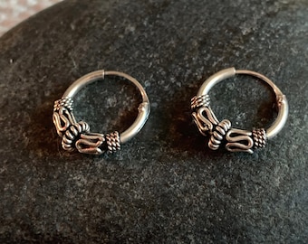 May include: A pair of silver hoop earrings with a detailed, intricate design. The hoops are small and delicate, and the design is made up of small, twisted wires.