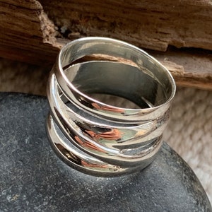 Pu&ograve; includere: Un anello d'argento con una fascia larga composta da pi&ugrave; fasce sovrapposte. L'anello &egrave; liscio e lucido.