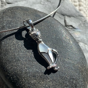 Può includere: Una collana a catena d'argento con un ciondolo a forma di gatto bianco e nero. Il gatto è fatto di madreperla e ha un contorno argentato.
