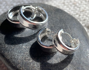 May include: Two silver hoop earrings with a smooth, rounded finish. The earrings are on a grey stone surface.