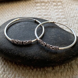 May include: A pair of silver hoop earrings with a decorative design. The hoops are smooth and have a small, intricate design on the front.