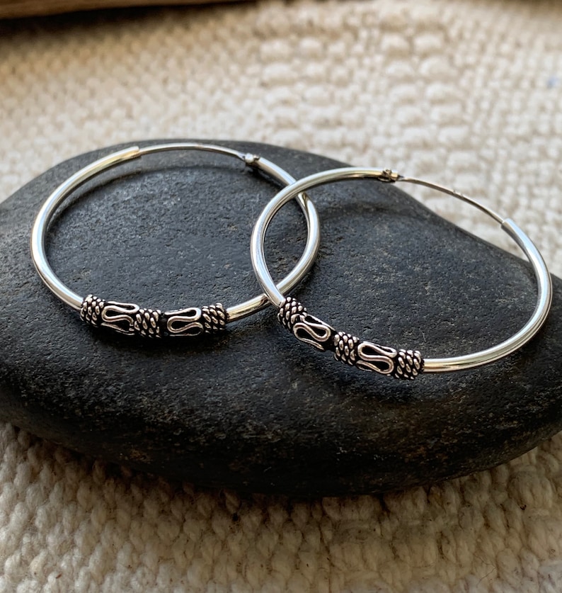 May include: A pair of silver hoop earrings with a decorative design. The hoops are smooth and have a small, intricate design on the front.