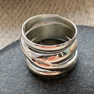 Pu&ograve; includere: Un anello d'argento con una fascia larga composta da pi&ugrave; strisce sovrapposte, curve e lucidate.