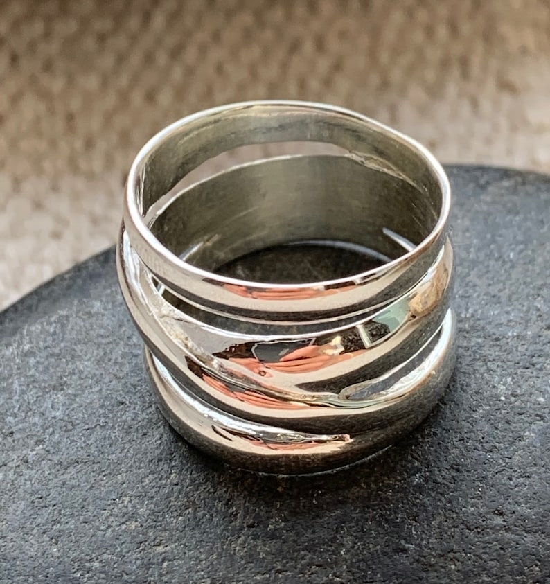 Pu&ograve; includere: Un anello d'argento con una fascia larga composta da pi&ugrave; strisce sovrapposte, curve e lucidate.
