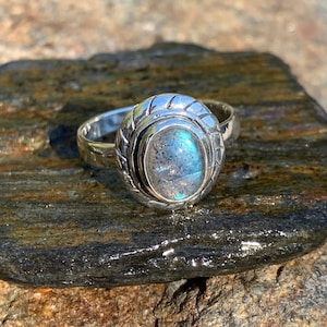 Peut inclure: Une bague en argent avec une pierre ovale en labradorite bleue et grise sertie dans une bande torsadée en argent.