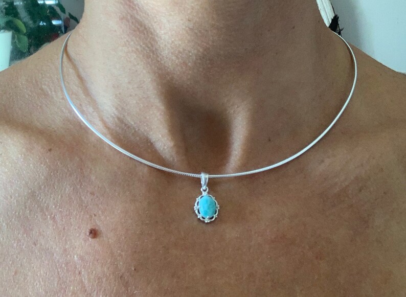 Op de afbeelding: Een zilveren ketting met een turquoise hanger. De hanger is ovaalvormig en heeft een zilveren frame.