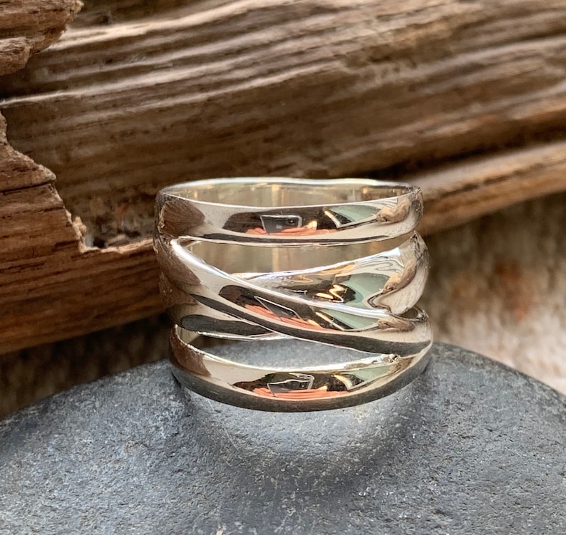 Pu&ograve; includere: Un anello d'argento con una fascia larga che presenta pi&ugrave; bande intrecciate. L'anello ha una finitura lucida e un design contemporaneo.