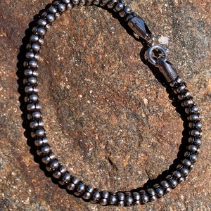 K&ouml;nnte beinhalten: Ein silbernes Armband mit Perlen und einem Karabinerverschluss.
