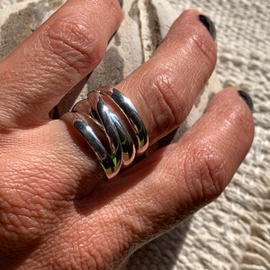 Pu&ograve; includere: Un anello d'argento con quattro bande intrecciate. L'anello &egrave; indossato su un dito.