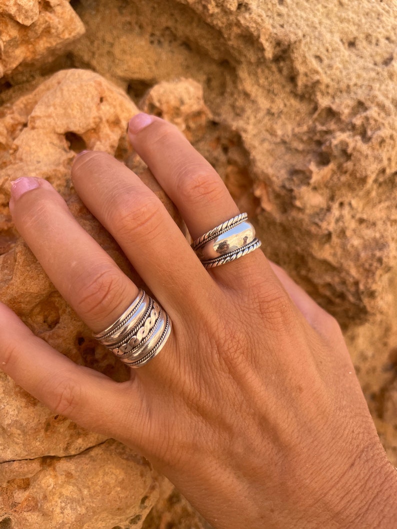 K&ouml;nnte beinhalten: Ein silberner Ring mit mehreren B&auml;ndern, jedes mit einem anderen strukturierten Design. Der Ring wird an einem Finger getragen.