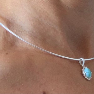 Op de afbeelding: Een zilveren ketting met een lichtblauwe ovale hanger. De hanger heeft een zilveren zetting.