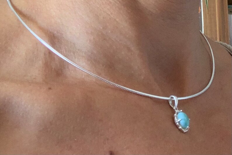 Op de afbeelding: Een zilveren ketting met een lichtblauwe ovale hanger. De hanger heeft een zilveren zetting.