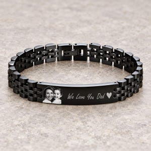 May include: A black metal link bracelet featuring a central rectangular plate. The plate is engraved with a photographic portrait of two people and the text We Love You Dad followed by a heart symbol. The bracelet has a secure clasp closure.