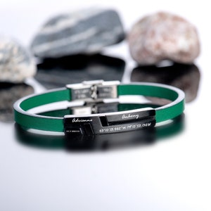 Puede incluir: Un brazalete de cuero verde con una placa de metal plateado grabada con los nombres "Adrienne" y "Anthony" y las coordenadas "43°10'13.462"N 79°15'53.364"W.